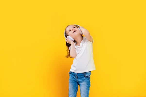 Chica escuchando música en auriculares inalámbricos sobre fondo amarillo. Bailarina. Feliz niña bailando música. Lindo niño disfrutando de música de baile feliz . — Foto de Stock