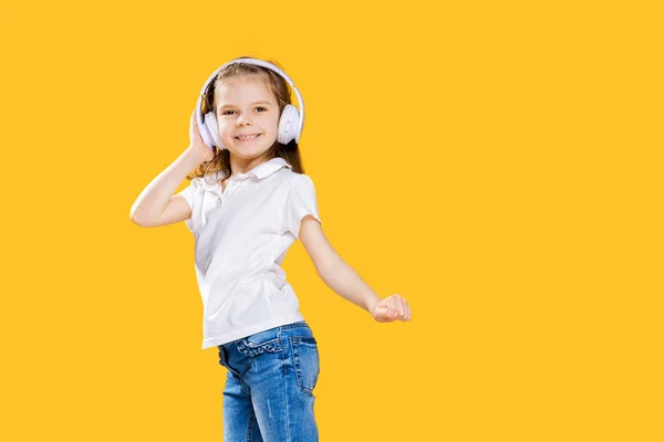 Chica escuchando música en auriculares inalámbricos sobre fondo amarillo. Bailarina. Feliz niña bailando música. Lindo niño disfrutando de música de baile feliz . — Foto de Stock