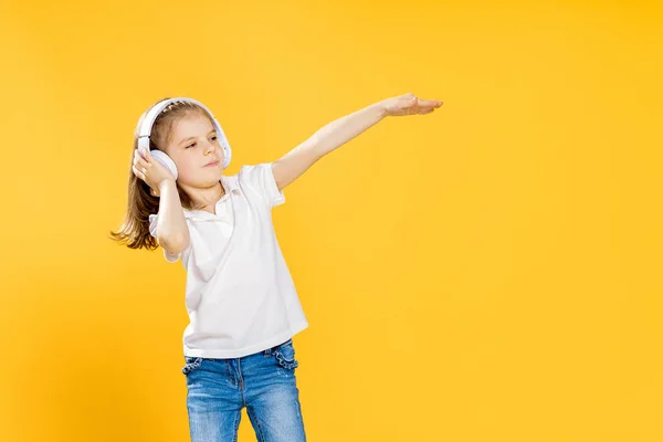 Chica escuchando música en auriculares inalámbricos sobre fondo amarillo. Bailarina. Feliz niña bailando música. Lindo niño disfrutando de música de baile feliz . — Foto de Stock