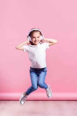 Kız pembe arka plan üzerinde kulaklık müzik dinliyor. Dans eden kız. Mutlu küçük kız müzikle dans ediyor. Sevimli çocuk mutlu dans müziği zevk.