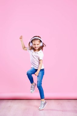 Kız pembe arka plan üzerinde kulaklık müzik dinliyor. Dans eden kız. Mutlu küçük kız müzikle dans ediyor. Sevimli çocuk mutlu dans müziği zevk.