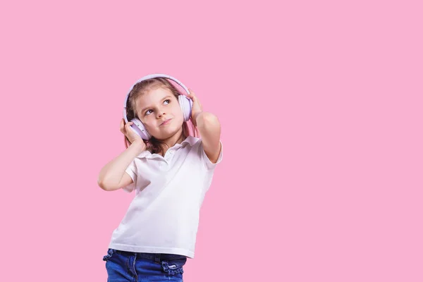 Dívka poslouchala hudbu ve sluchátkách na růžovém pozadí. Milé dítě, které si vychutnávají šťastnou taneční muziku, oči a usměje se na pozadí ve studiu — Stock fotografie