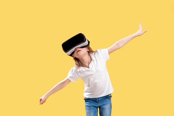 여자 7 y.o 정장 의상을 입고 VR 안경을 쓰고 노란 배경에 고립 된 흥분에 손을 내미고. 가상 현실을위한 게임 가젯을 사용하는 어린이. 가상 기술 — 스톡 사진