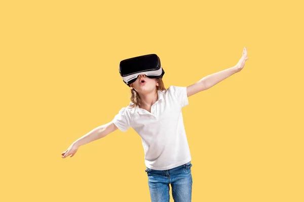 여자 7 y.o 정장 의상을 입고 VR 안경을 쓰고 노란 배경에 고립 된 흥분에 손을 내미고. 가상 현실을위한 게임 가젯을 사용하는 어린이. 가상 기술 — 스톡 사진