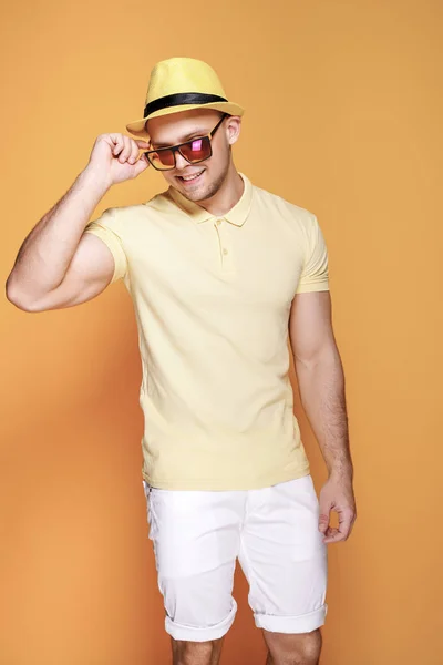 Zelfverzekerd stijlvolle kerel in geel shirt, zonnebril, witte shorts, stro hoed op zoek zijde weg van camera — Stockfoto