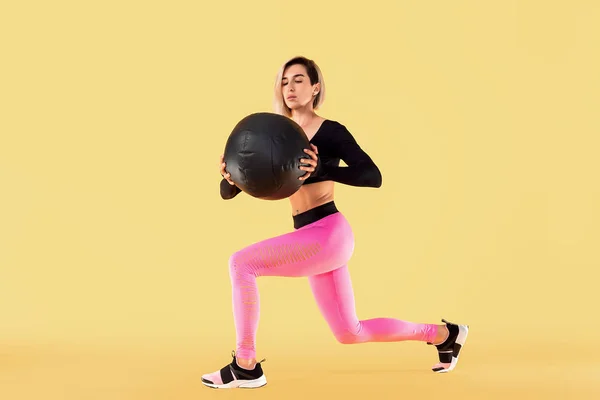 Exercício de mulher forte com bola de medicina. Foto de mulher latina desportiva na moda sportswear no fundo amarelo . — Fotografia de Stock