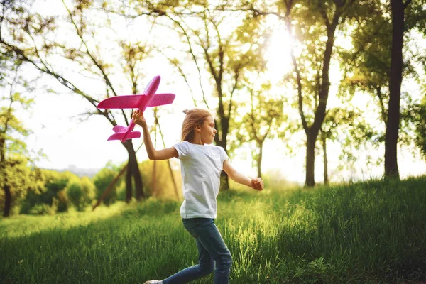 Kislány, játszani egy játék síkon a levegőben a parkban. Gyermek indít játék síkon. Szép kislány, fuss a füvön, és elindítja a rózsaszín játék sík — Stock Fotó