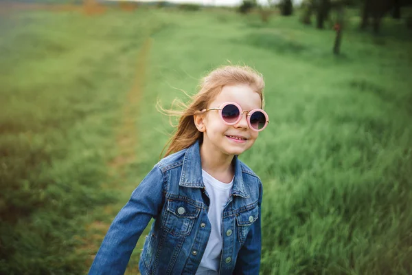Feliz divertido hermosa niña en gafas de sol en verde verano naturaleza campo puesta del sol fondo — Foto de Stock