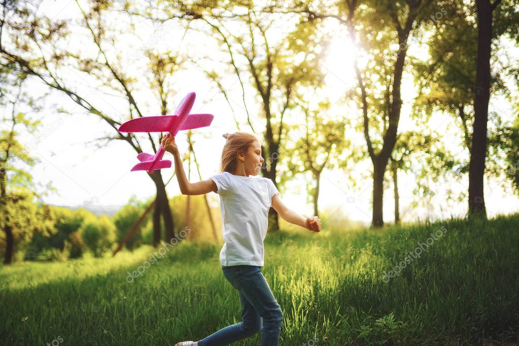 Little girl, play with a toy plane in the air in park. Child launches a toy plane. Beautiful little girl, run on the grass and launches a pink toy plane