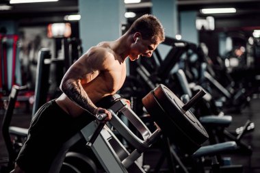 Strong Bodybuilder Doing Heavy Weight Exercise For Back On Machine. T-pull exercise