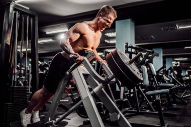 Strong Bodybuilder Doing Heavy Weight Exercise For Back On Machine. T-pull exercise