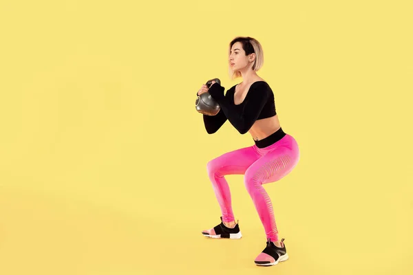 Mulher fitness na moda rosa e preto sportswear trabalhar com kettlebell no fundo amarelo . — Fotografia de Stock