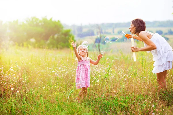 Мать и маленькая девочка дочь ребенок дует мыльные пузыри на открытом воздухе. Родители и дети веселятся на лугу. Счастливое и беспечное детство. Хорошие семейные отношения — стоковое фото