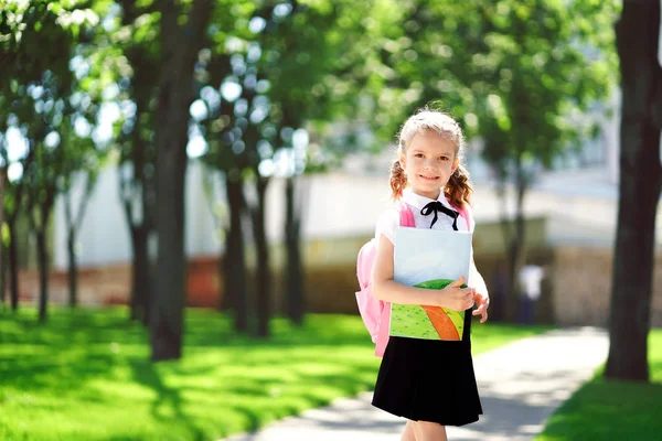 Χαμογελαστή μαθήτρια με σχολική τσάντα και βιβλίο ασκήσεων. Πορτρέτο ενός ευτυχισμένου καυκάσιου κοριτσιού έξω από το δημοτικό. Χαμογελαστή μαθήτρια κοιτάζοντας την κάμερα. — Φωτογραφία Αρχείου