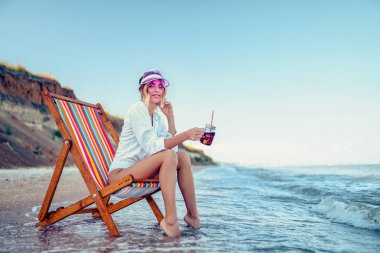 Güzel bir kadın plajda dinleniyor ve soda içiyor. yaz tatili konsepti