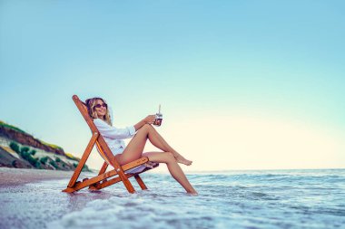 Güzel bir kadın plajda dinleniyor ve soda içiyor. yaz tatili konsepti