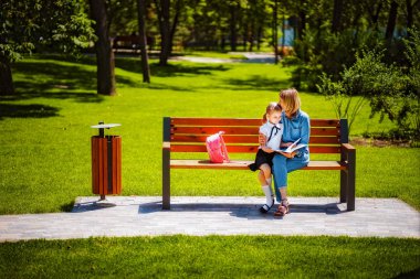 Anne ve küçük kızı açık havada halka açık parkta bankta oturan ve kitap okumak, çalışma dersleri. Ebeveynlik ve çocuk kavramı