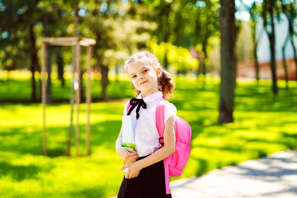 Χαμογελαστή μαθήτρια με σχολική τσάντα και βιβλίο ασκήσεων. Πορτρέτο ενός ευτυχισμένου καυκάσιου κοριτσιού έξω από το δημοτικό. Χαμογελαστή μαθήτρια κοιτάζοντας την κάμερα — Φωτογραφία Αρχείου