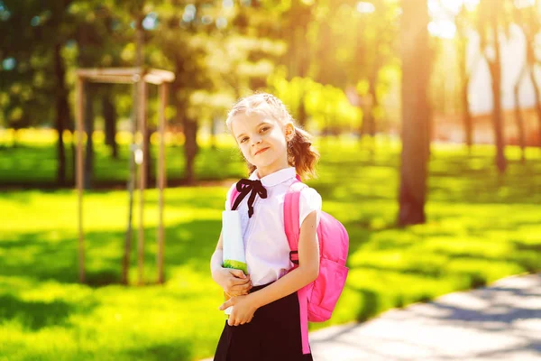 Χαμογελαστή μαθήτρια με σχολική τσάντα και βιβλίο ασκήσεων. Πορτρέτο ενός ευτυχισμένου καυκάσιου κοριτσιού έξω από το δημοτικό. Χαμογελαστή μαθήτρια κοιτάζοντας την κάμερα — Φωτογραφία Αρχείου