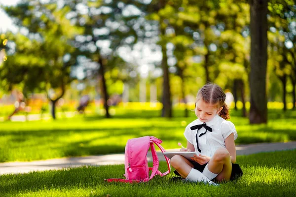 Μικρό σχολείο κορίτσι με ροζ σακίδιο κάθεται σε γρασίδι μετά από μαθήματα και να διαβάσετε το βιβλίο ή σπουδές μαθήματα, σκέψης ιδέες, εκπαίδευση και μάθηση αντίληψη — Φωτογραφία Αρχείου