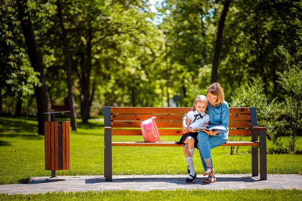 Mãe e filha pequena no parque público ao ar livre sentado no banco e ler livro, estudar aulas. Conceito de paternidade e filho — Fotografia de Stock