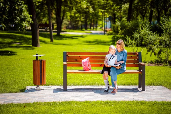 Mãe e filha pequena no parque público ao ar livre sentado no banco e ler livro, estudar aulas. Conceito de paternidade e filho — Fotografia de Stock