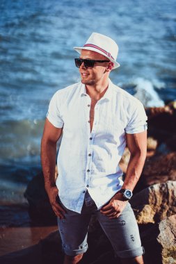 Tatil beldesinde bir gömlek, güneş gözlüğü ve şapka deniz arka plan üzerinde adam