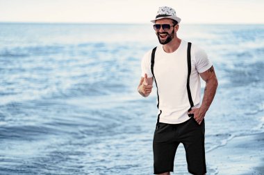 Bir gömlek mavi ve güneş gözlüğü, deniz arka planda şapka ile tatil de adam