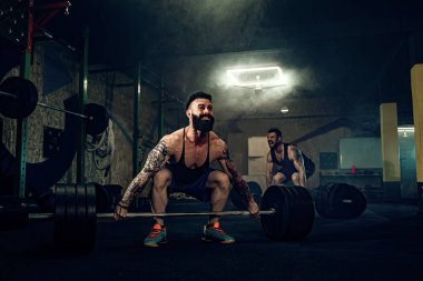 İki kaslı sakallı sporcu spor salonunda antrenman yapıyor.