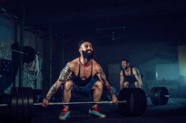 İki kaslı sakallı sporcu spor salonunda antrenman yapıyor.