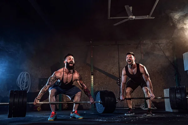 Zwei muskulöse bärtige tätowierte Athleten beim Training im Fitnessstudio — Stockfoto