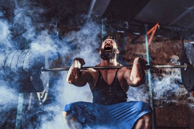 Modern fitness merkezinde kaslı bir fitness adamı halterle kafasına halteri indiriyor. Fonksiyonel eğitim.
