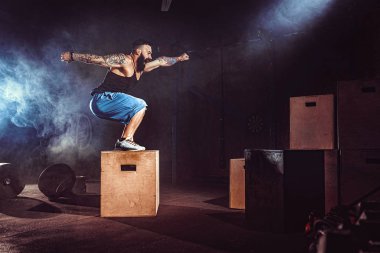 Sporcu egzersiz yaptı. Kutunun üstüne atlamak. İniş aşaması. Koyu tonda jimnastik atışları. İç..