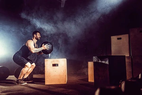 Fit tätowierte bärtige Mann springen auf eine Box als Teil der Übung Routine. Mann beim Boxsprung in der Turnhalle. Athlet macht Box-Sprünge — Stockfoto
