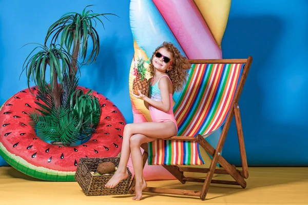 Girl in swimwear and sunglasses sitting in rainbow deck chair — Stock Photo, Image