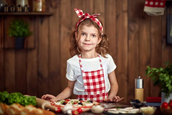 Söt flicka i rutig förkläde matlagning pizza — Stockfoto
