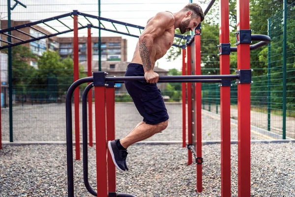 Hombre musculoso fuerte haciendo flexiones en bares irregulares en el gimnasio de la calle al aire libre — Foto de Stock