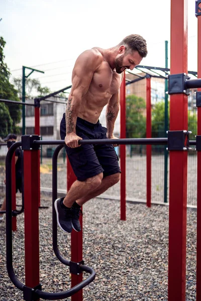 Starker muskulöser Mann macht Liegestütze auf unebenem Stufenbarren in Outdoor-Street-Gym — Stockfoto