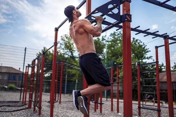 Starker muskulöser Mann macht Liegestütze auf unebenem Stufenbarren in Outdoor-Street-Gym — Stockfoto