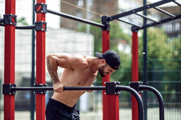 Homem musculoso forte fazendo flexões em bares irregulares no ginásio de rua ao ar livre — Fotografia de Stock