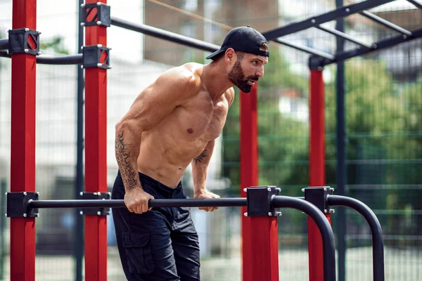 Hombre musculoso fuerte haciendo flexiones en bares irregulares en el gimnasio de la calle al aire libre —  Fotos de Stock