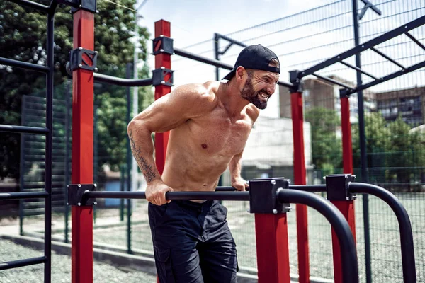 Hombre musculoso fuerte haciendo flexiones en bares irregulares en el gimnasio de la calle al aire libre —  Fotos de Stock