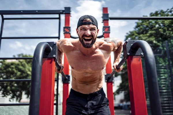 Starker muskulöser Mann macht Liegestütze auf unebenem Stufenbarren in Outdoor-Street-Gym — Stockfoto