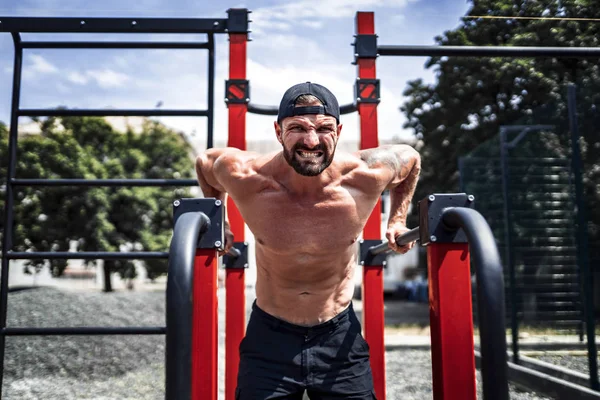 Starker muskulöser Mann macht Liegestütze auf unebenem Stufenbarren in Outdoor-Street-Gym — Stockfoto