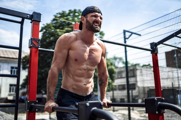 Starker muskulöser Mann macht Liegestütze auf unebenem Stufenbarren in Outdoor-Street-Gym — Stockfoto