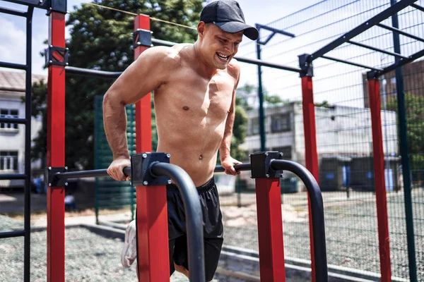 Hombre musculoso fuerte haciendo flexiones en bares irregulares en el gimnasio de la calle al aire libre — Foto de Stock