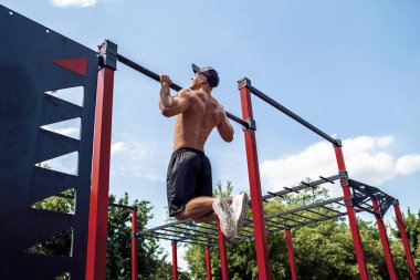 Brutal athletic man making pull-up exercises on a crossbar. clipart