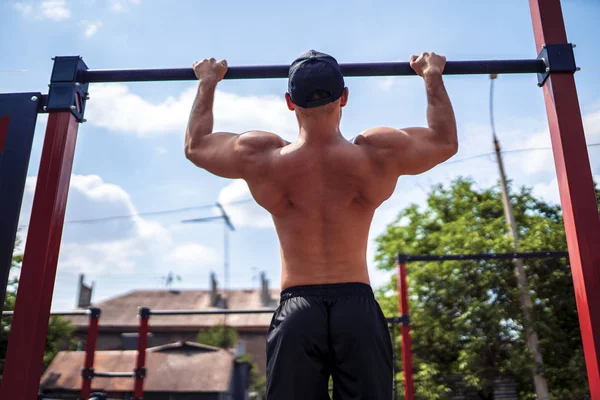 Brute atletische man het maken van pull-up oefeningen op een dwarsbalk. — Stockfoto