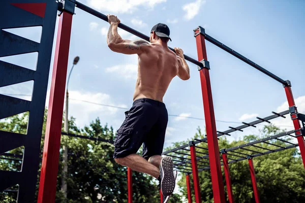Homem atlético brutal fazendo exercícios pull-up em uma barra transversal . — Fotografia de Stock