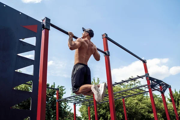 Hombre atlético brutal haciendo ejercicios pull-up en un travesaño . — Foto de Stock